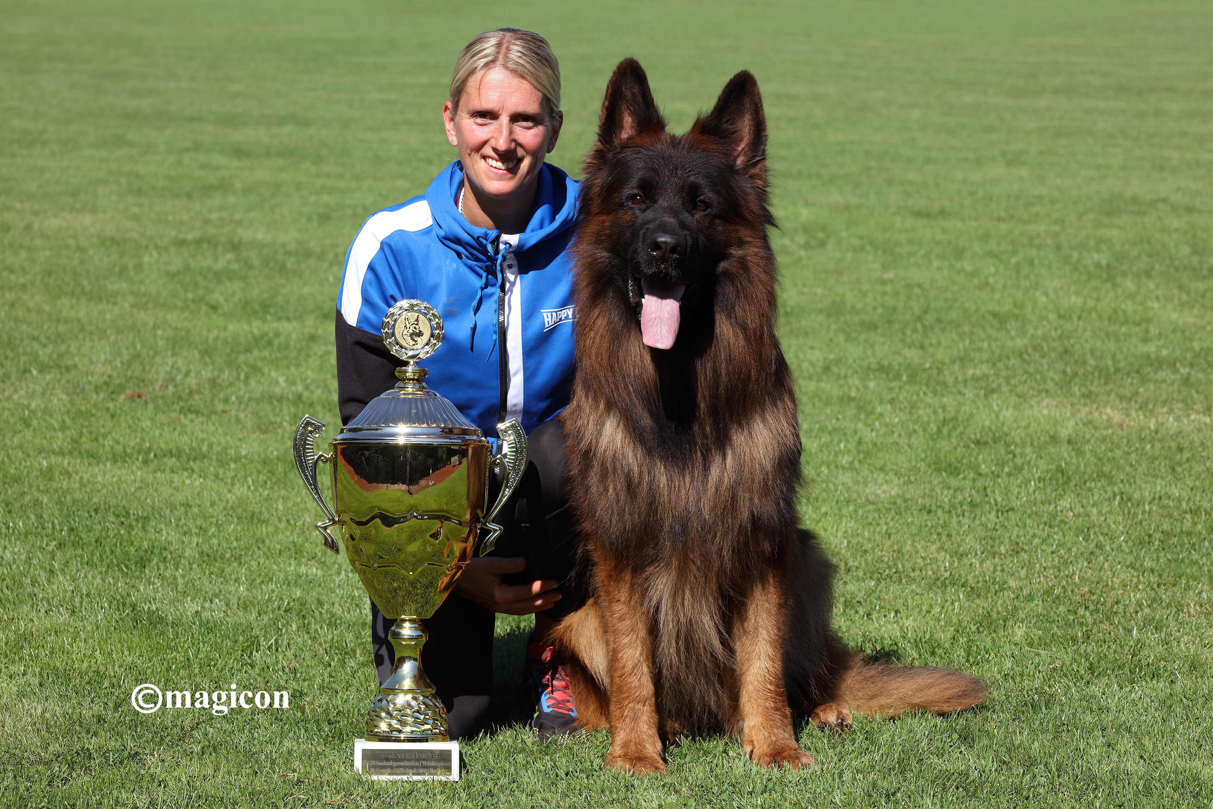 Schäferhund mit Pokal und Frauchen auf einer Wiese