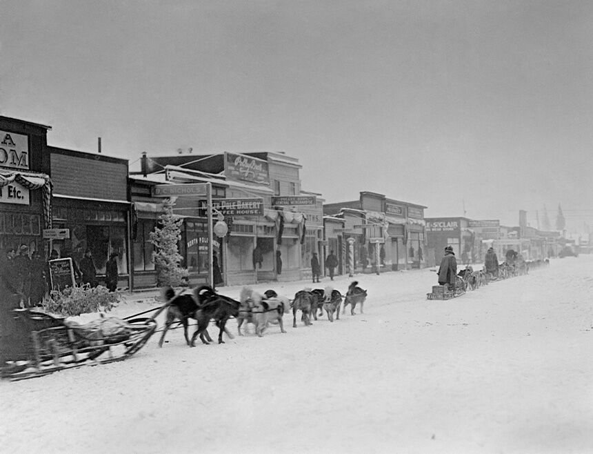 Historisches schwarz-weiß Bild von Schlittenhunden, die eine Schlitten durch die Stadt ziehen