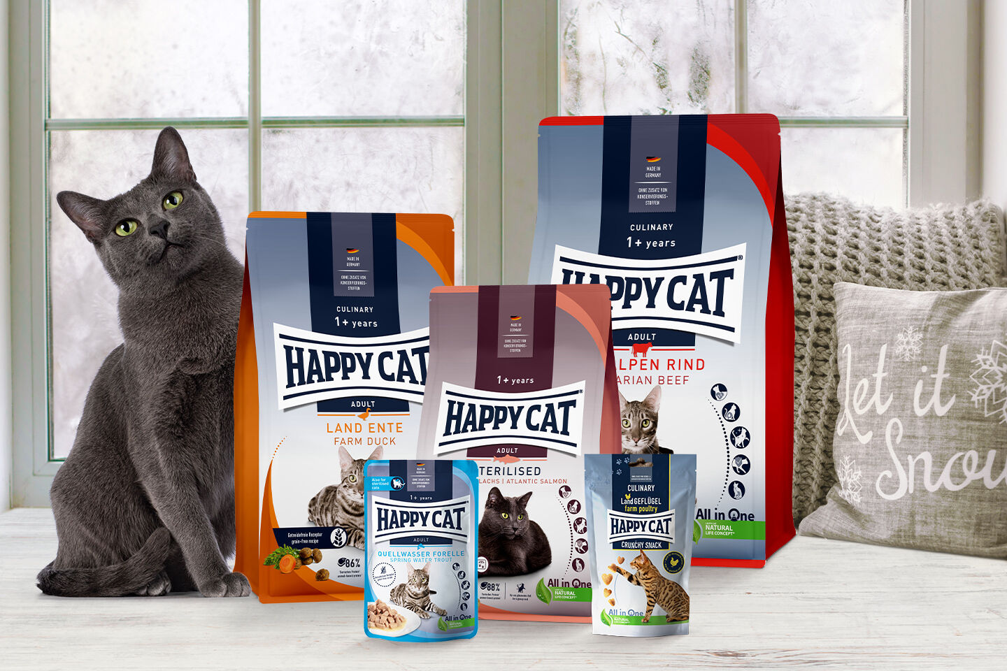 Eine Katze siegt neben Futtersäcken von Happy Cat.