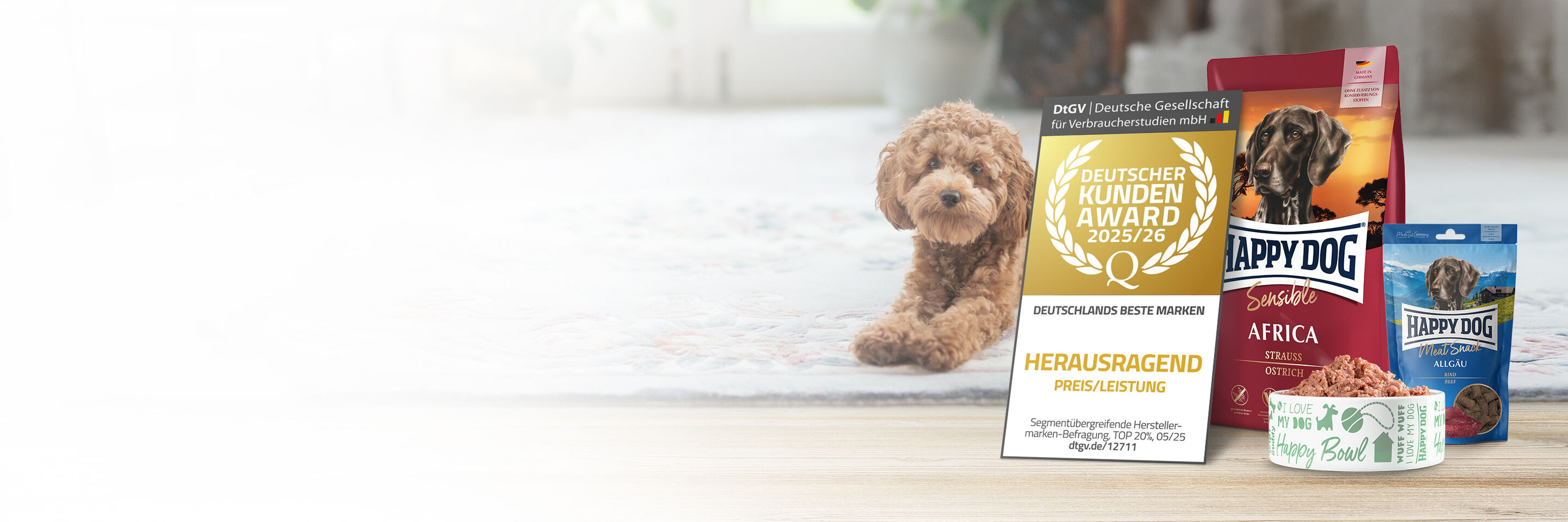 Ein brauner Pudel liegt auf dem Teppich neben Happy Dog Futter und der Auszeichnung Deutscher Kundenaward 2025