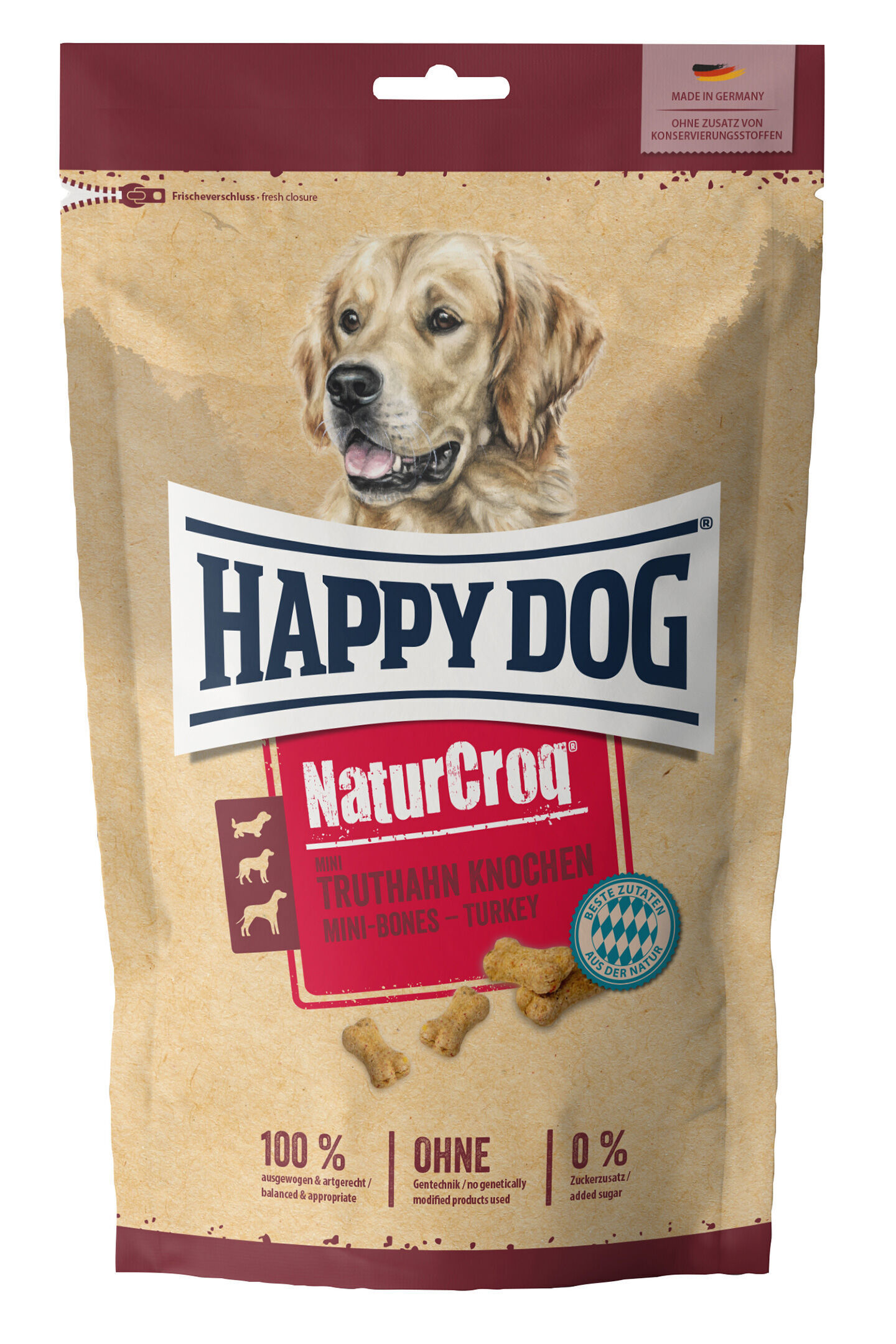 Verpackung von Happydog Hundesnacks mit Truthahn-Mini-Knochen auf braunem Hintergrund. Texte: "Made in Germany", "Ohne Zusatz von Konservierungsstoffen", "100% ausgewogen", "Ohne Gentechnik", "0% Zuckerzusatz".