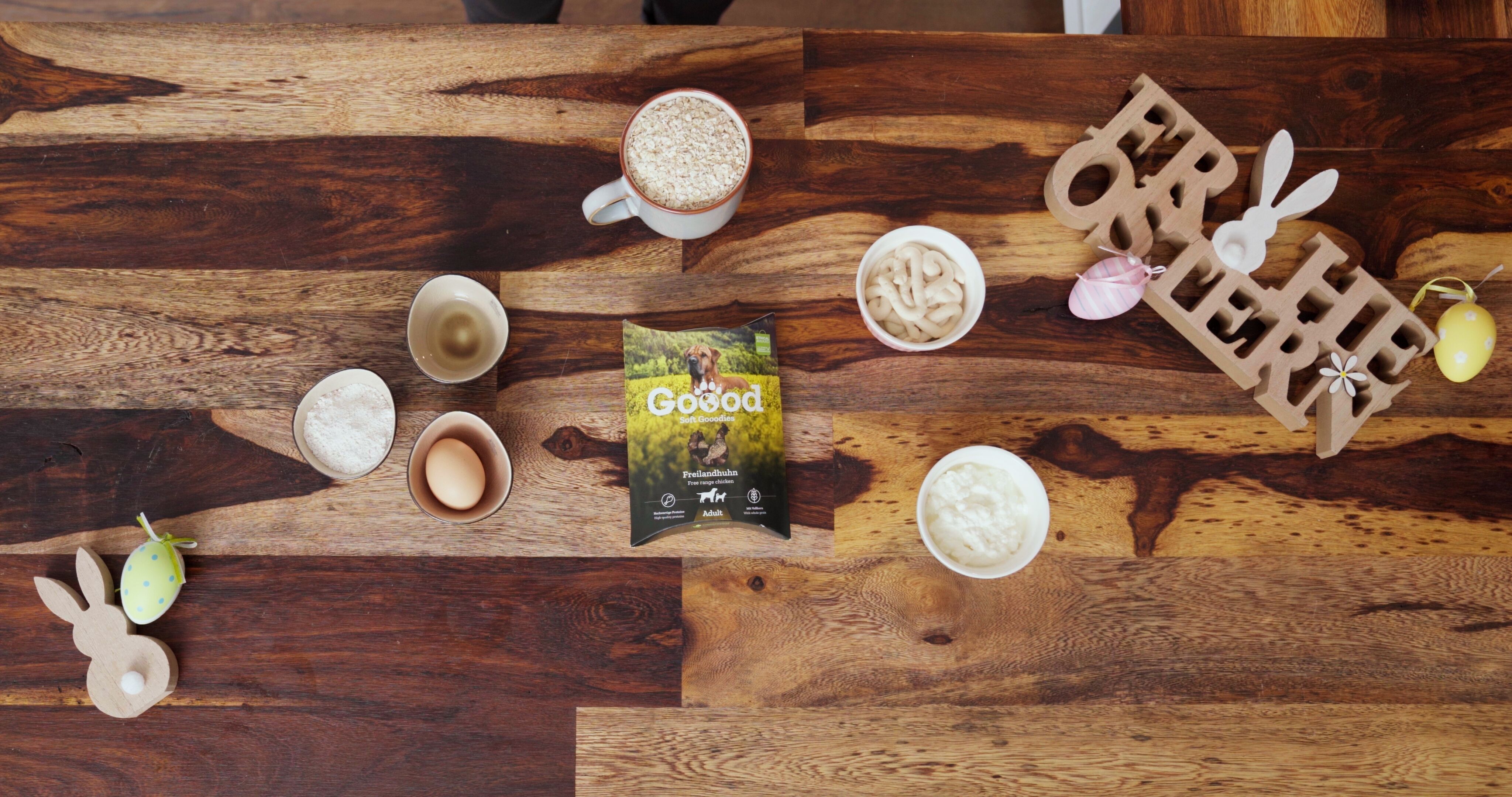 Zutaten zum Backen von Osterkeksen und Goood Hunde Leckerlis liegen auf einem Holztische, der mit Osterdekoration geschmückt ist.