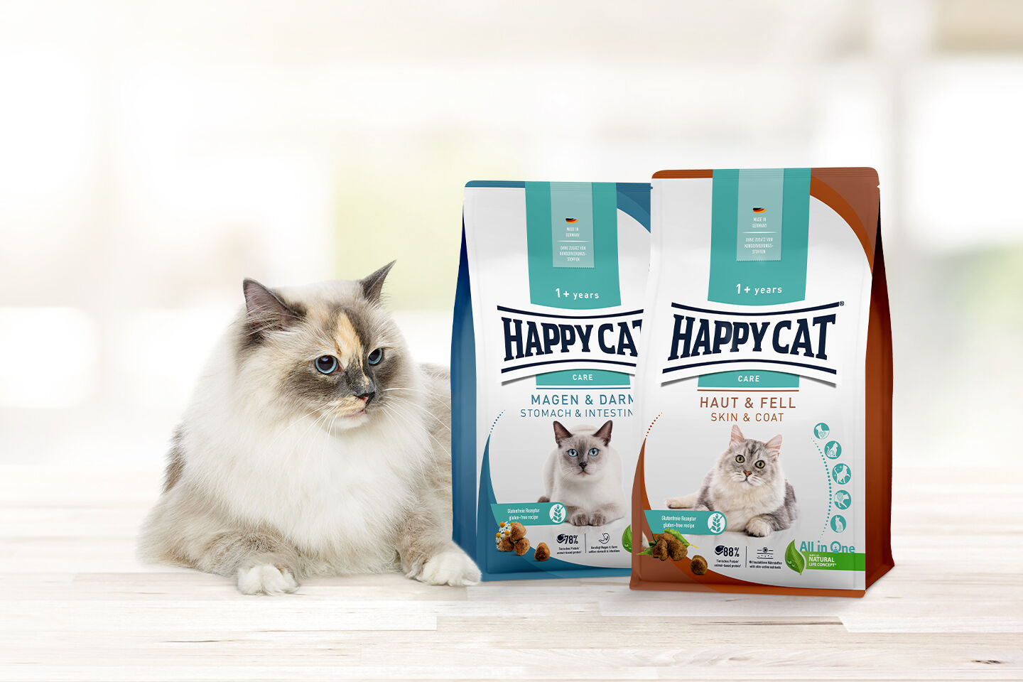 Eine weiße Katze liegt neben zwei Happy Cat Trockenfutter Packungen.