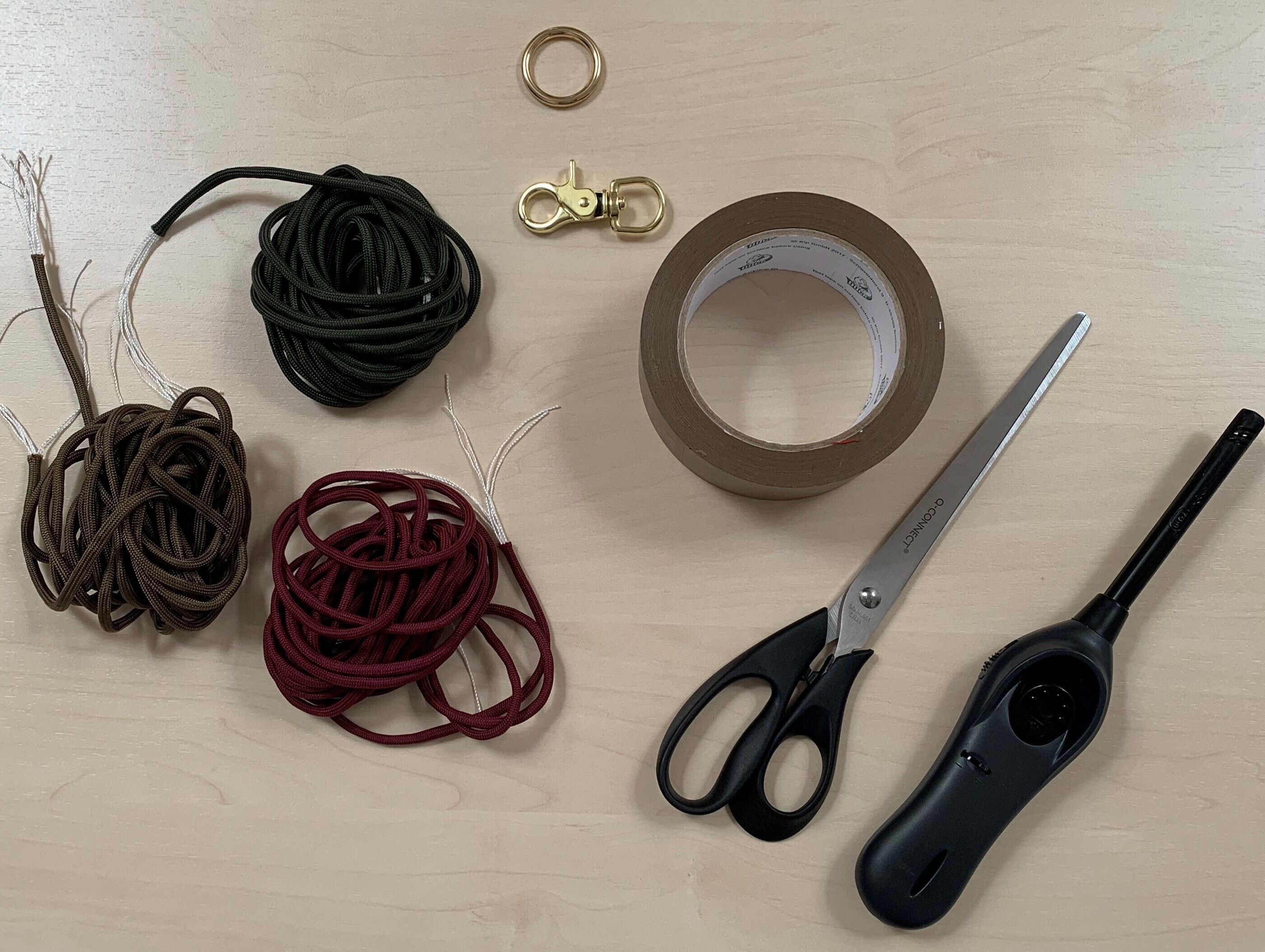 Schnüre, Klebeband, eine Schere, ein Feuerzeug und ein Verschluss für ein Hundehalsband liegen auf einem Holztisch.