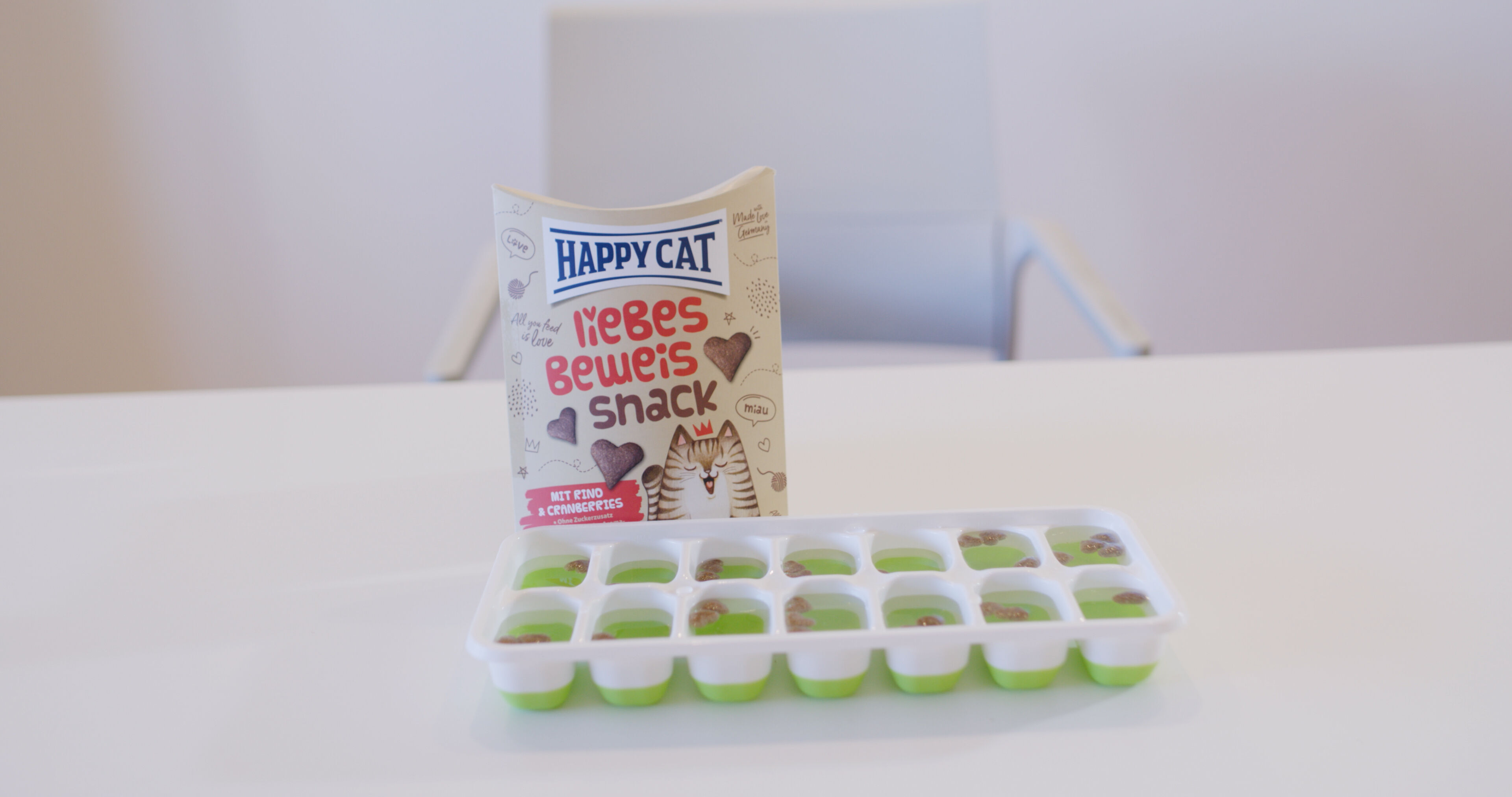 Eine Leckerli Packung für Katzen von Happy Cat steht auf einem Tisch hinter einer Eiswürfelform.
