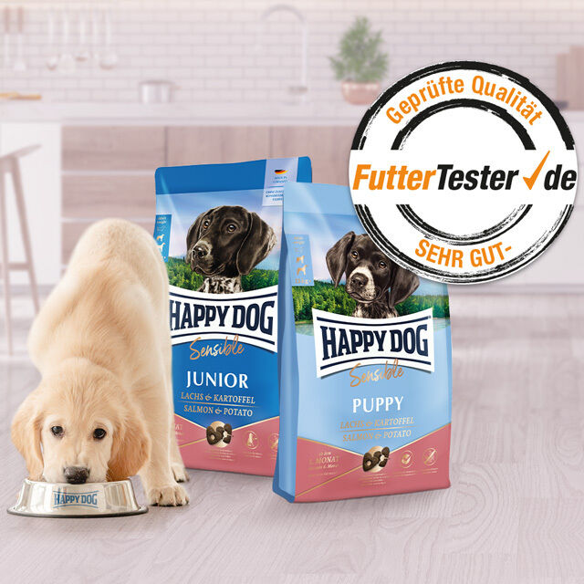 Ein Hund frisst aus einem Napf, neben ihm steht eine Dose Nassfutter von Happy Dog. Darüber ist eine Auszeichnung abgebildet.