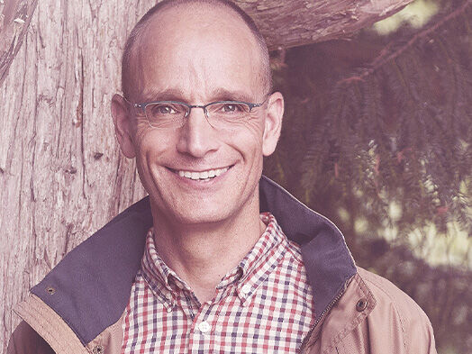 Geschäftsführer Georg Müller steht lächelnd vor einem Baum.