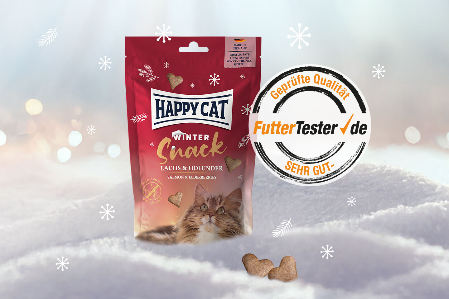 Die Verpackung von "Happy Cat Winter Snack" für Katzen mit "Lachs & Holunder" liegt im Schnee. Auf dem Etikett: "Made in Germany", "Geprüfte Qualität FutterTester.de SEHR GUT".