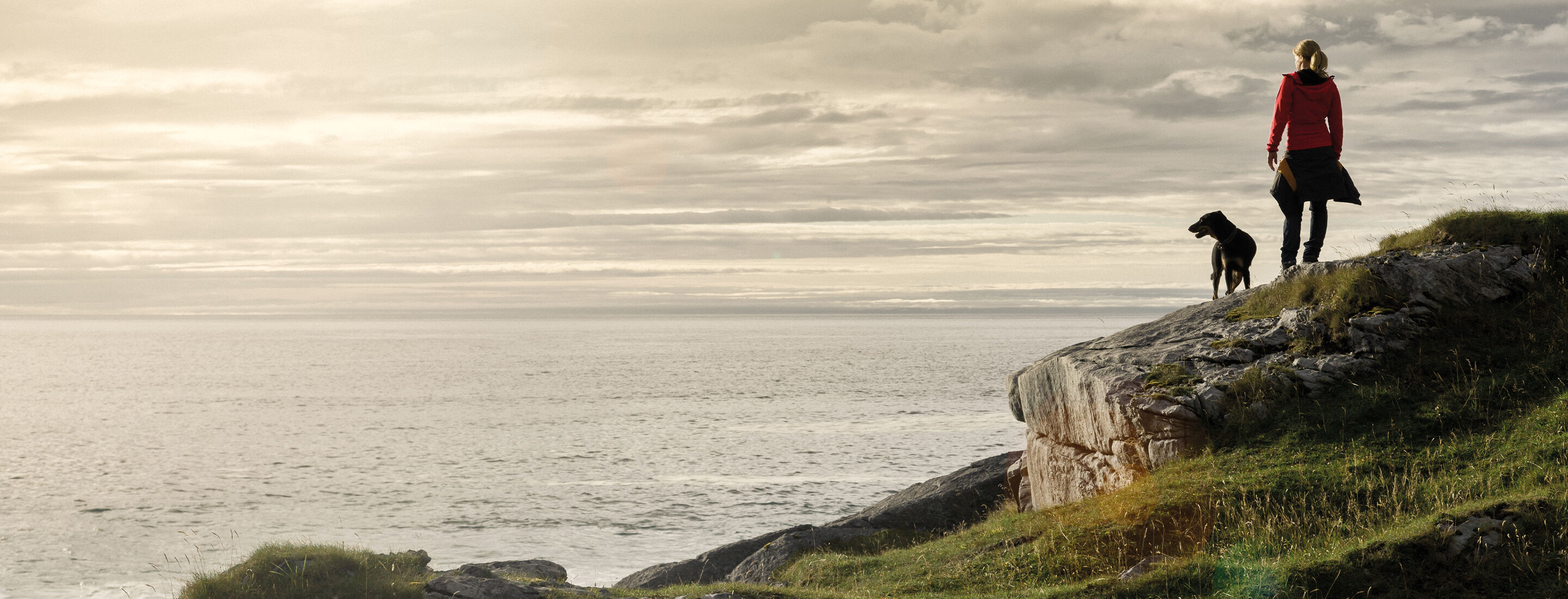 Eine Frau und ihr Hund gehen am Meer spazieren.
