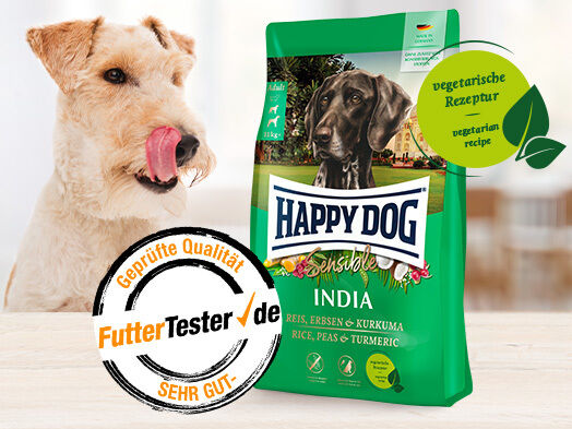 Ein Hund schaut einen Futtersack von Happy Dog Sensible India an. Die Auszeichnung von FutterTester mit der Note Sehr Gut ist beigefügt.