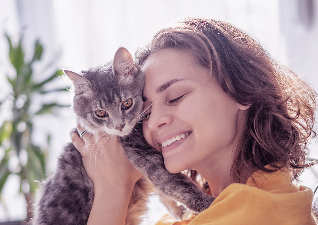 Lächelnde Frau hält Katze vor ihr Gesicht und schmust mit ihr