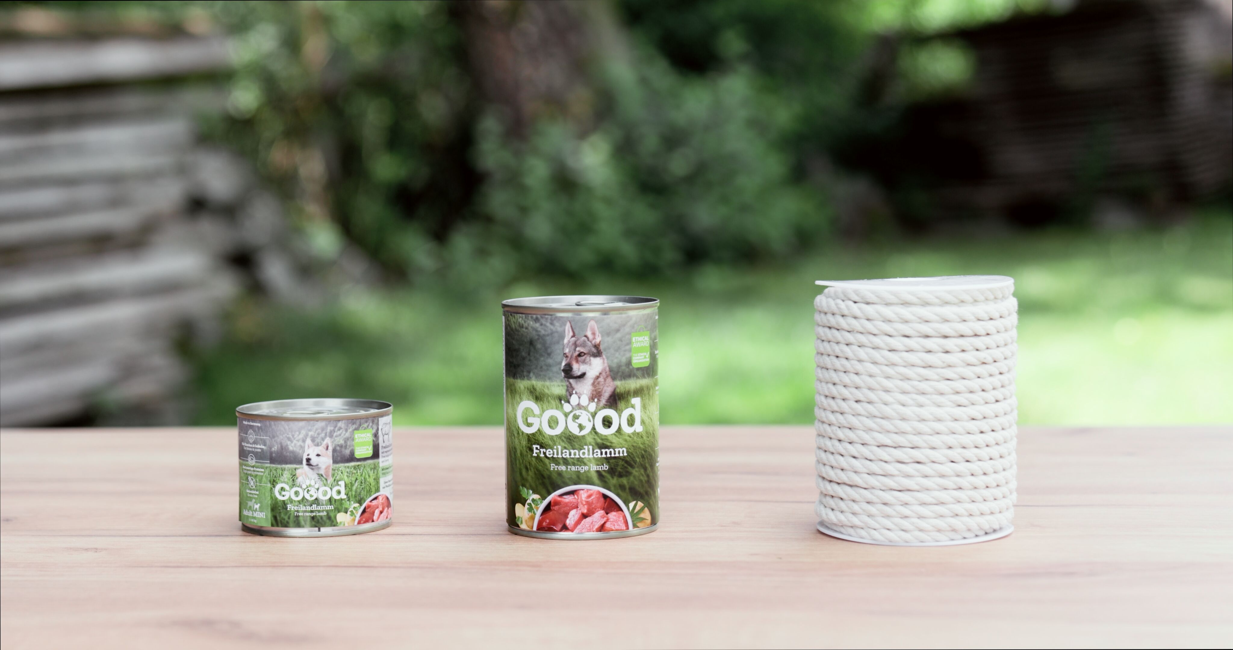 Eine kleine und eine große Hundefutterdose von Goood sowie Kord steht auf einem Holztisch.