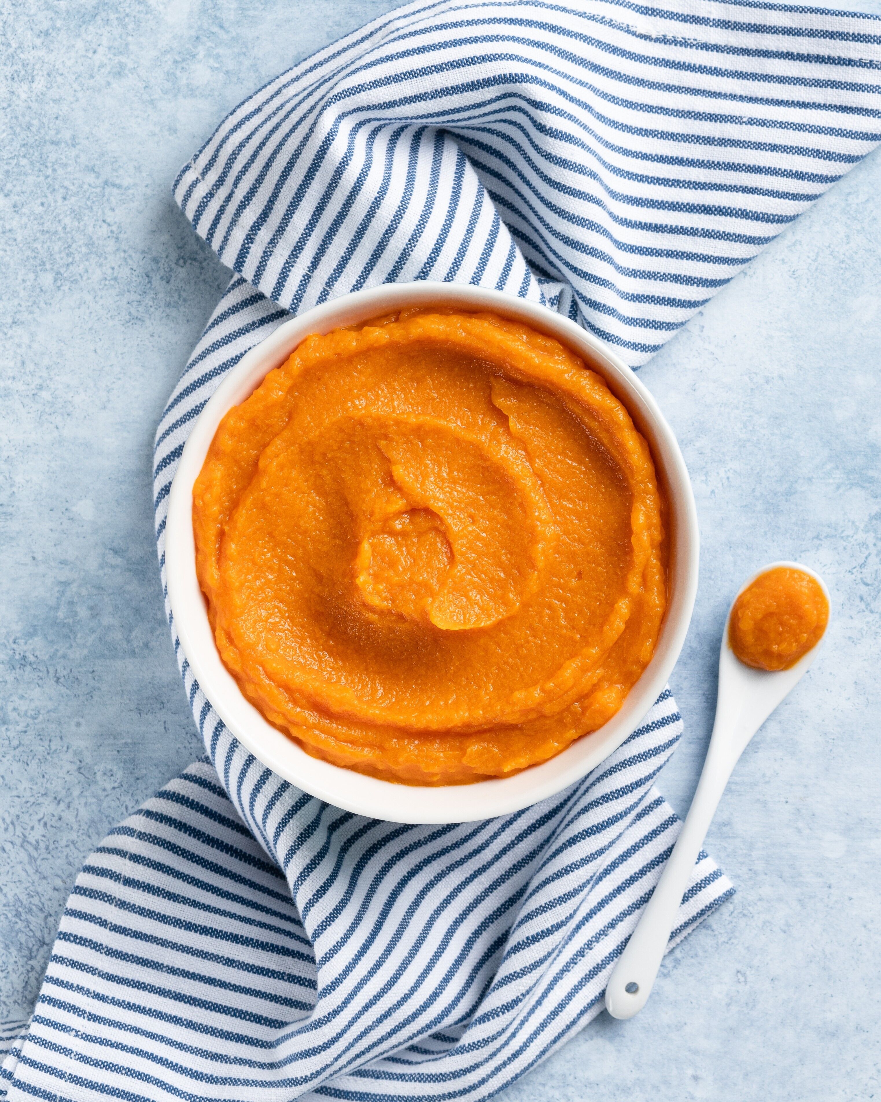 Weißer Teller mit Kürbissuppe auf weiß-blau gestreiftem Handtuch und blauem Hintergrund