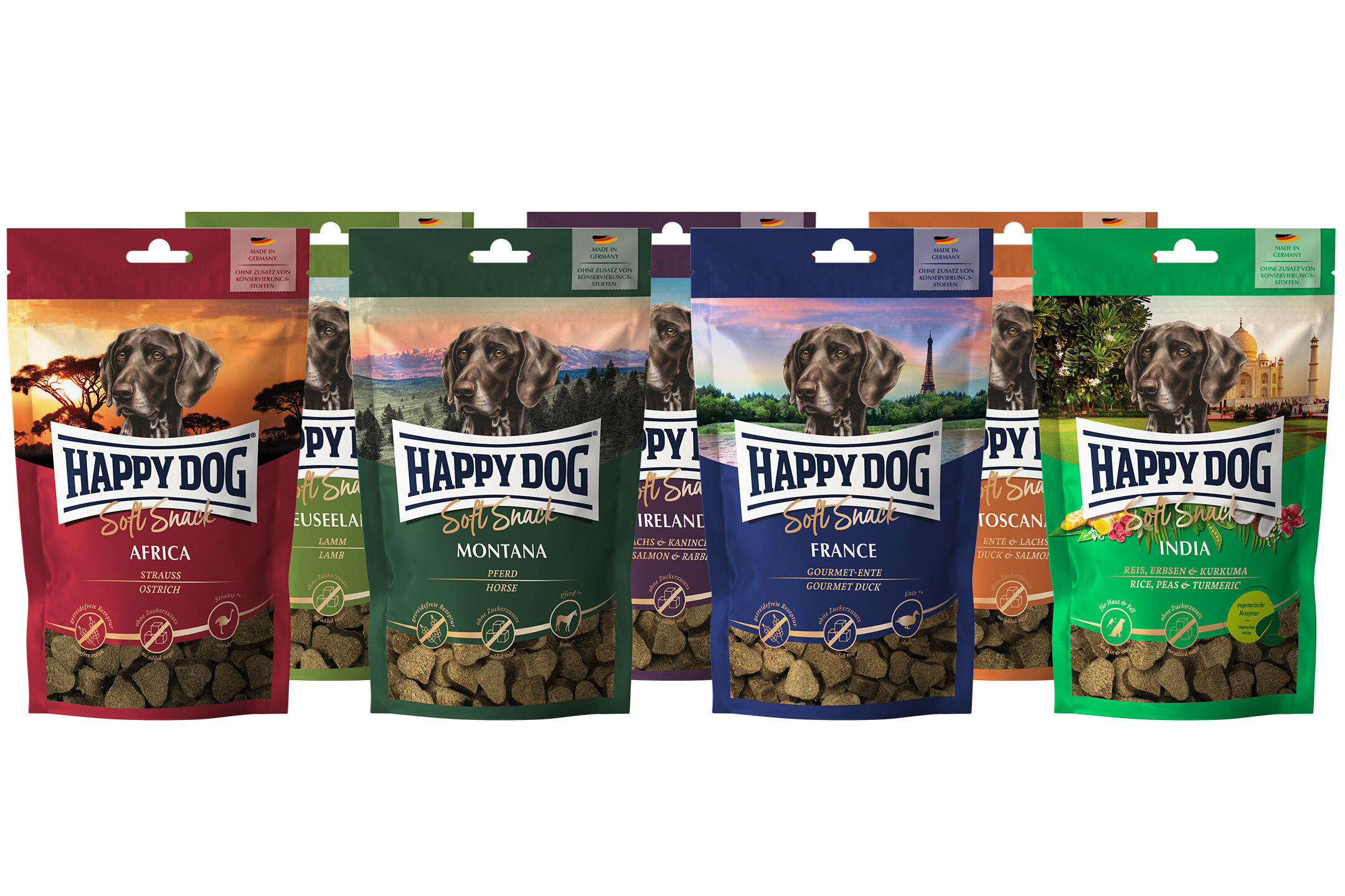 Soft Snack Probierpaket Sechs bunte Tüten Happy Dog Soft Snacks in verschiedenen Geschmacksrichtungen, jeweils mit Hundebild und Landschaft im Hintergrund, stehen nebeneinander. Text: Happy Dog Soft Snack.