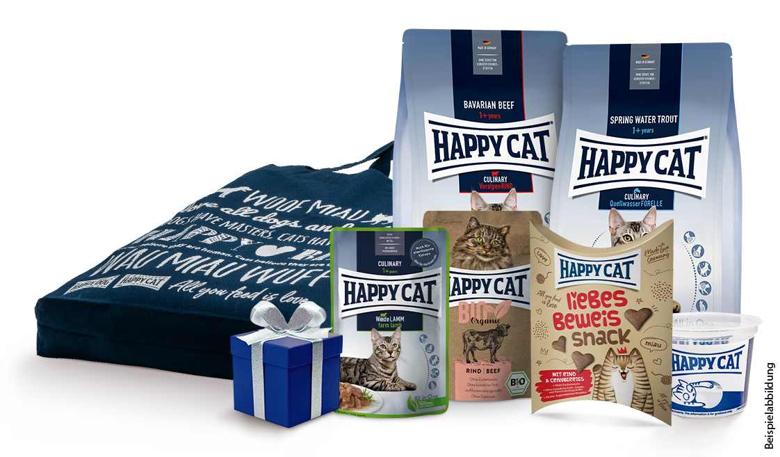 Ein blaues Geschenkpaket mit Schleife liegt vor mehreren Happy Cat Verpackungen für Katzenfutter und Snacks in unterschiedlichen Sorten und Größen. Text auf einer Verpackung: "Woof Mau".
