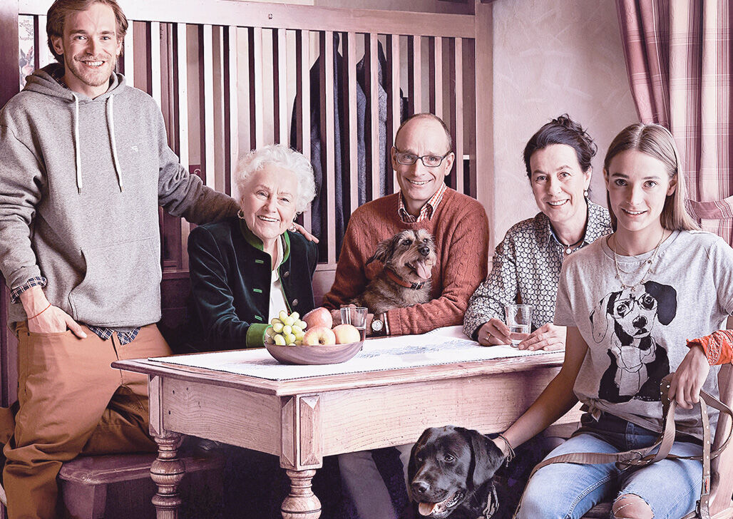 Familienbild der Müllers, die gemeinsam mit zwei Hunden um einen Tisch sitzen bzw. stehen.